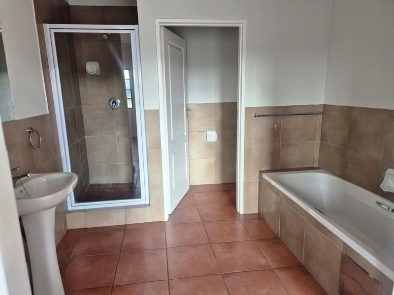 A functional bathroom featuring a pedestal basin, a separate shower enclosure, and a built-in bathtub with neutral tiled finishes throughout.