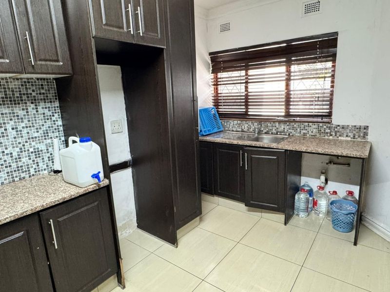 Kitchen featuring dark wood cabinetry, granite countertops, and mosaic tile backsplash. The space requires minor repairs to cabinetry and finishes.