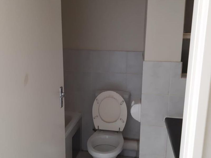 A compact bathroom featuring a standard toilet, tiled flooring, and wall tiling, presenting a functional space in need of cosmetic updates.