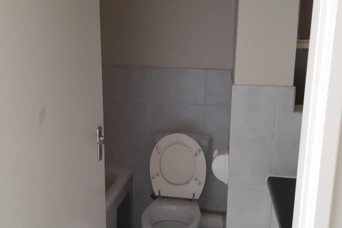A compact bathroom featuring a standard toilet, tiled flooring, and wall tiling, presenting a functional space in need of cosmetic updates.