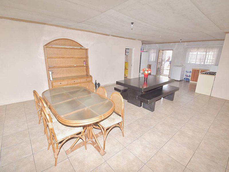 Spacious open-plan living and dining area featuring tiled flooring and a functional kitchen space with built-in cabinetry and stove.
