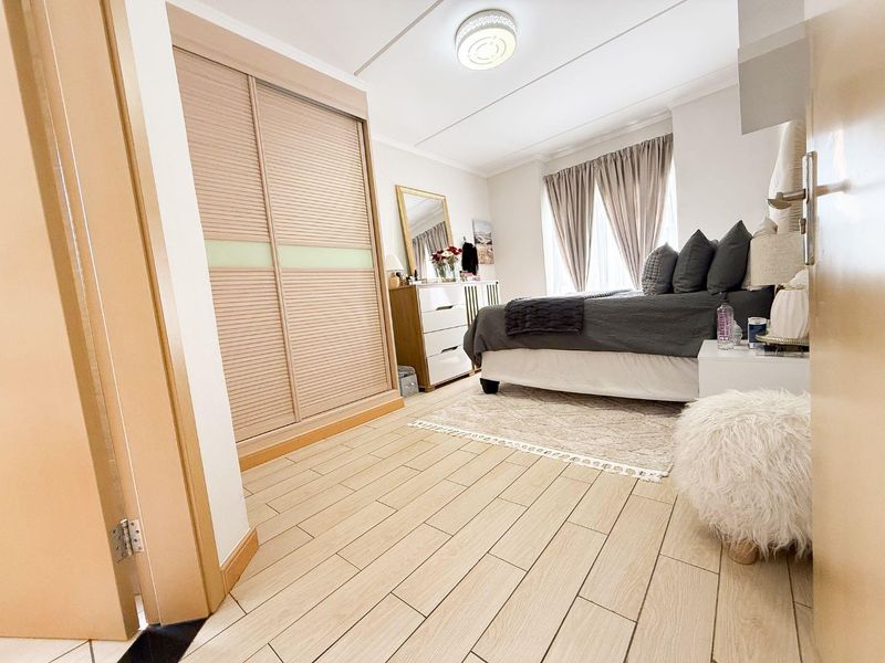 A well-maintained bedroom featuring light wood-look tiled flooring, a large built-in wardrobe with sliding doors, and a neutral color palette.