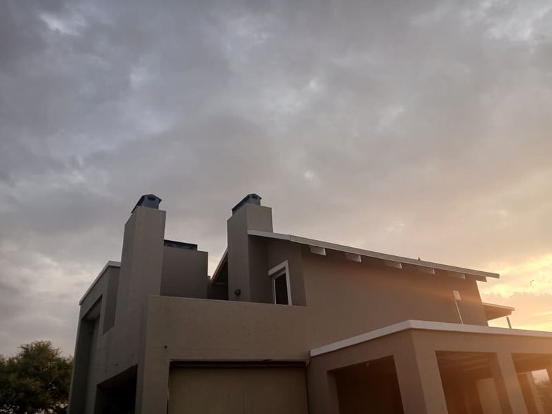 A view of the rear exterior elevation of the apartment building, featuring prominent chimney stacks and a pitched roofline against a cloudy sky.