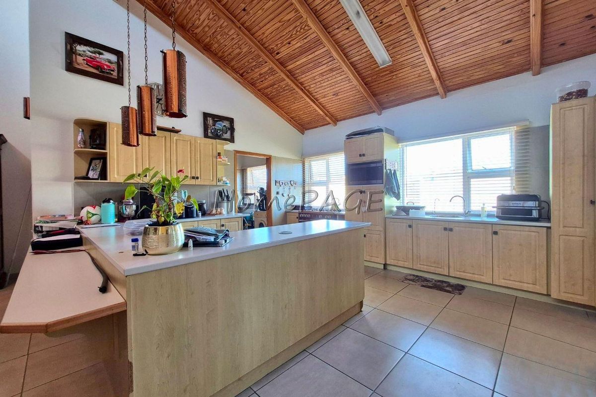 Spacious kitchen featuring a large central island, timber vaulted ceilings, tiled flooring, and ample built-in cabinetry with integrated storage solutions.