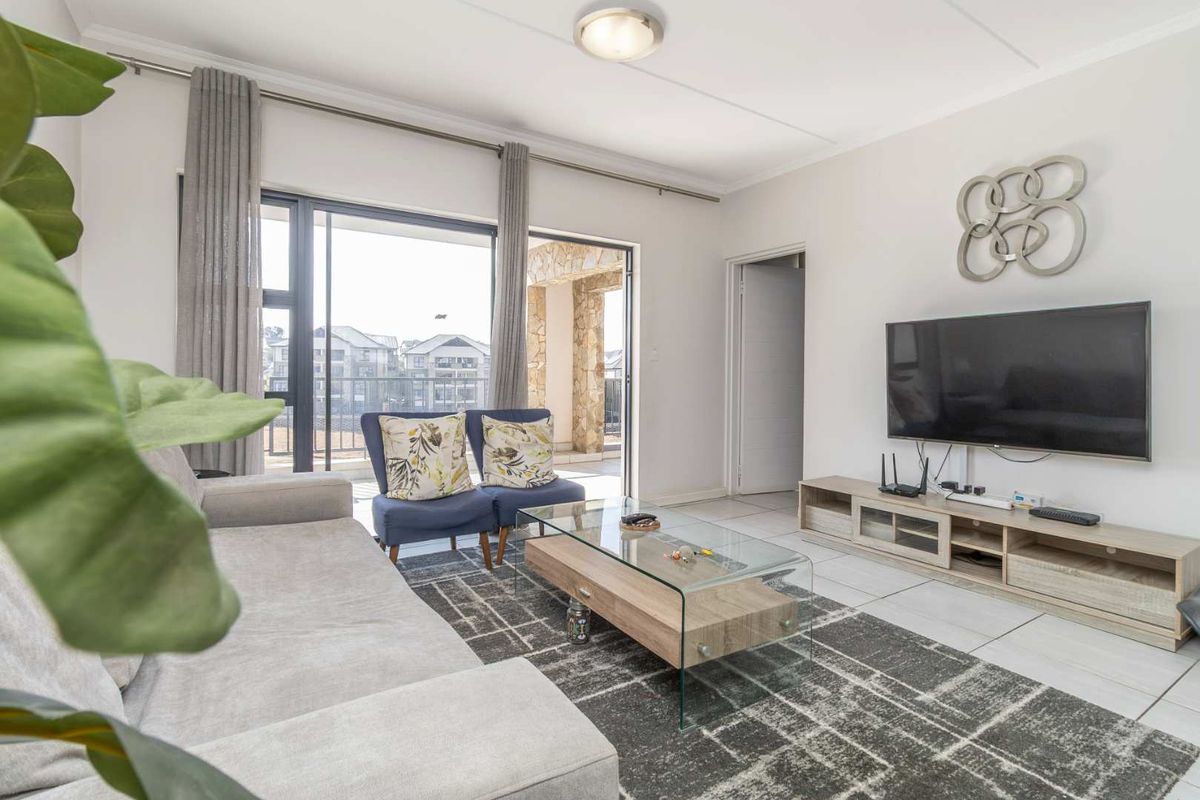A bright living room featuring tiled flooring and a large sliding glass door that provides access to an outdoor balcony area.