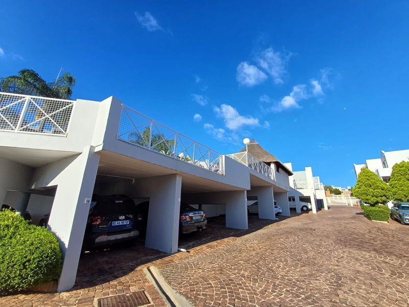 A view of the apartment complex featuring covered parking bays with concrete structures and paved driveway access.