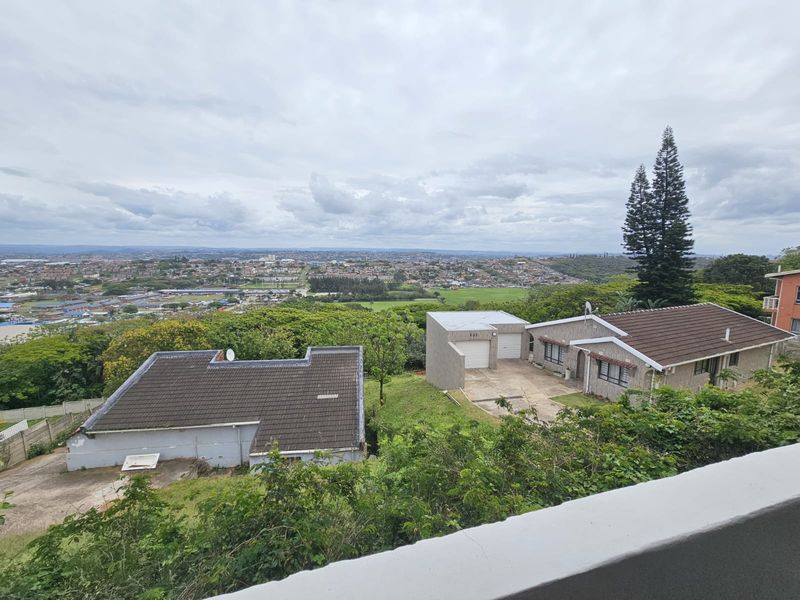 An elevated aerial view of the property showing the main house, detached garage, and surrounding residential landscape with a distant city view.