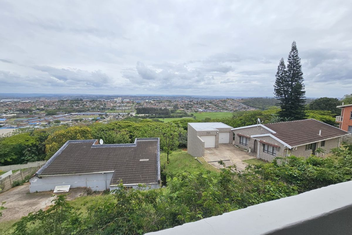An elevated aerial view of the property showing the main house, detached garage, and surrounding residential landscape with a distant city view.
