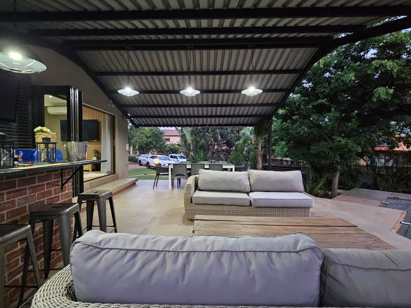 A spacious covered patio featuring a built-in brick bar, tiled flooring, and integrated lighting, perfect for outdoor entertaining and relaxation.