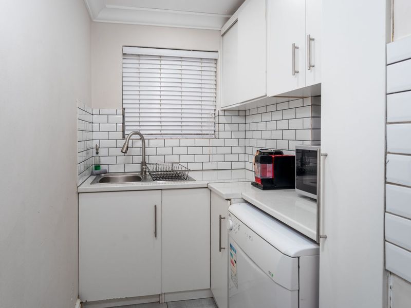 A compact and functional scullery featuring white cabinetry, stone countertops, a subway tile backsplash, and a modern gooseneck faucet.