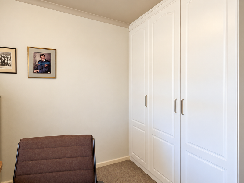 A well-maintained bedroom featuring neutral walls, carpeted flooring, and ample storage provided by a large, white built-in wardrobe.