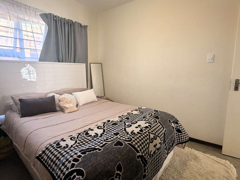A standard bedroom featuring tiled flooring and a window fitted with security bars.