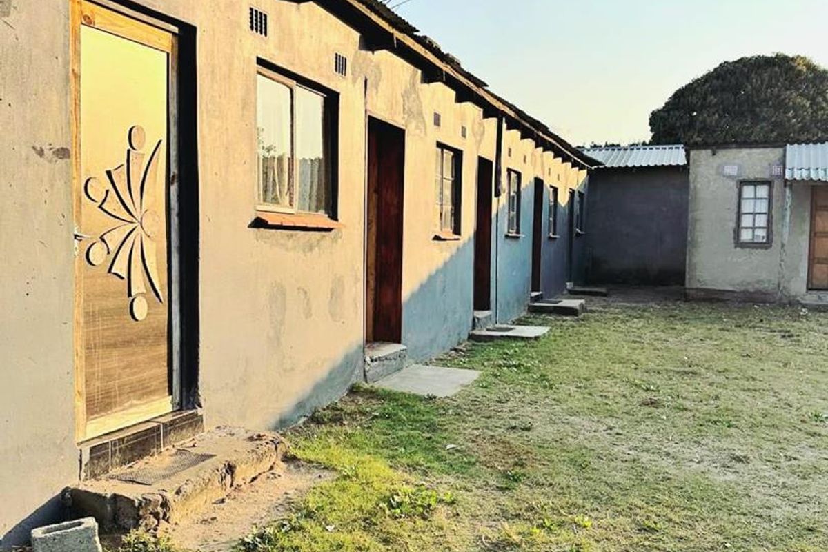 Rear view of a multi-unit residential building featuring a row of individual entrances with concrete steps and corrugated metal roofing.