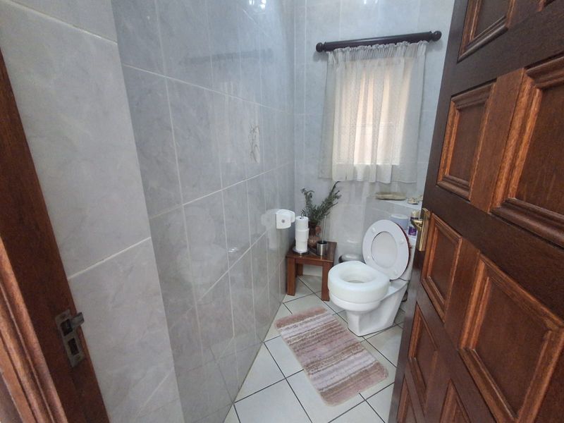 A compact bathroom featuring full-height ceramic wall tiling, tiled flooring, and a standard toilet suite.