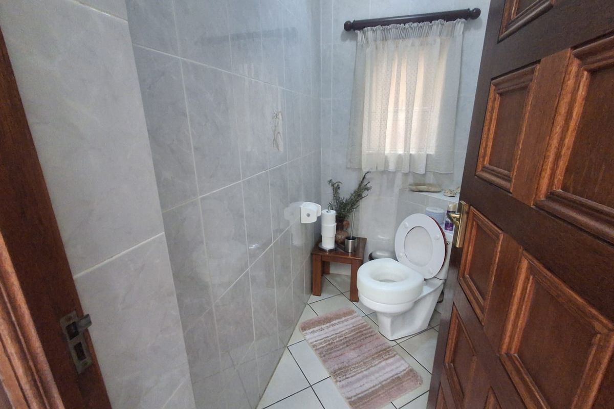 A compact bathroom featuring full-height ceramic wall tiling, tiled flooring, and a standard toilet suite.