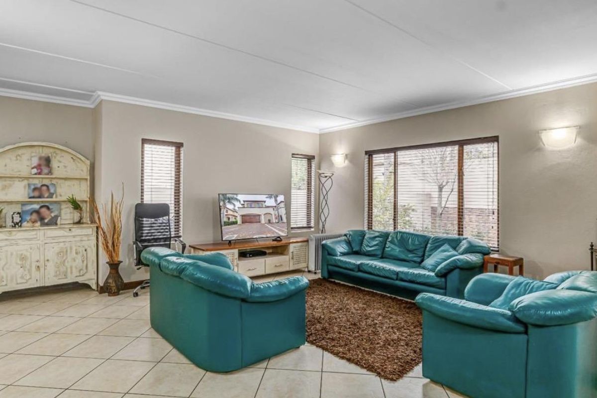 Spacious living room featuring neutral wall tones, tiled flooring, and large windows with fitted blinds, providing ample natural light.