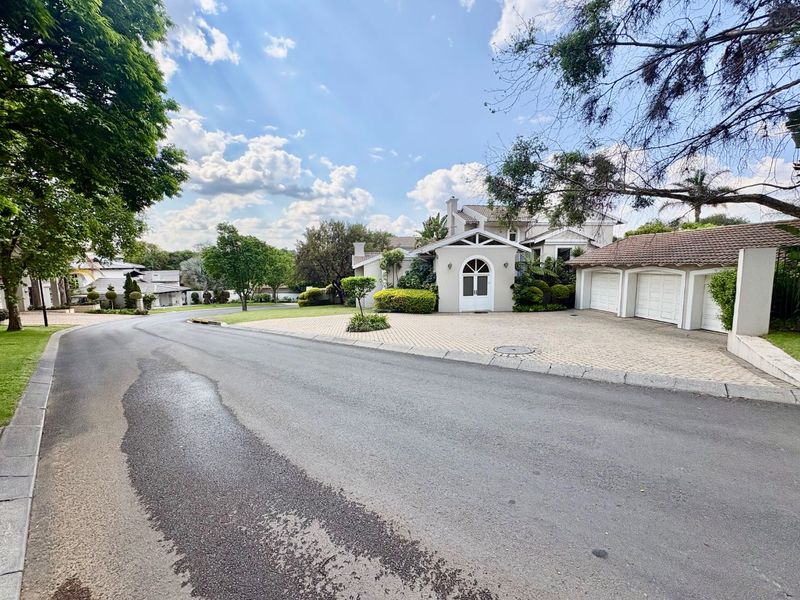 A street-level view of a well-maintained residential property featuring a paved driveway, triple garage, and an arched entrance in a quiet neighborhood.