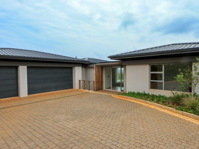 Modern front exterior featuring a paved driveway, double garage, and clean architectural lines with timber accents and landscaped garden beds.