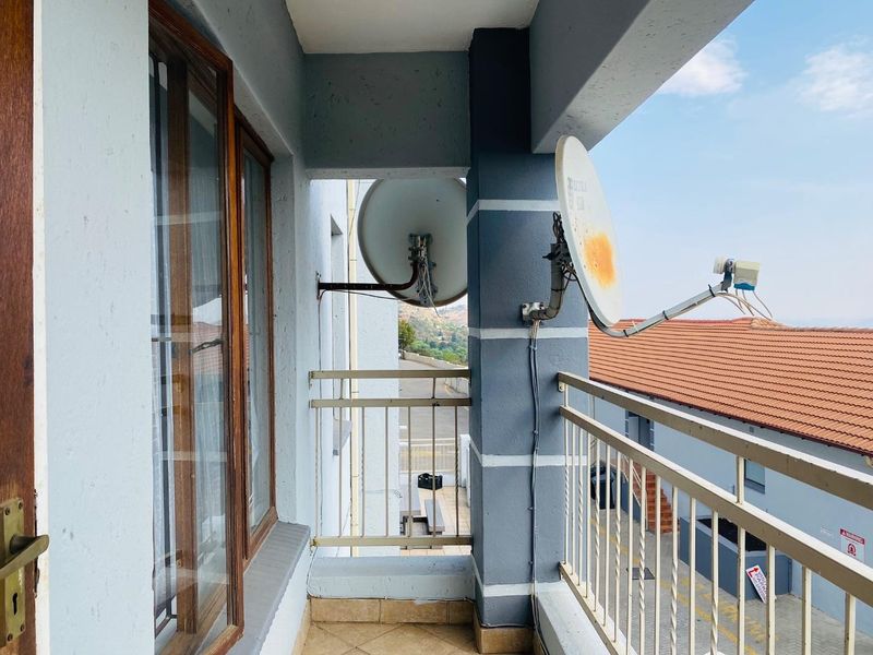 A functional balcony area featuring tiled flooring, a metal balustrade, and wooden window frames, offering an elevated view of the surrounding complex.