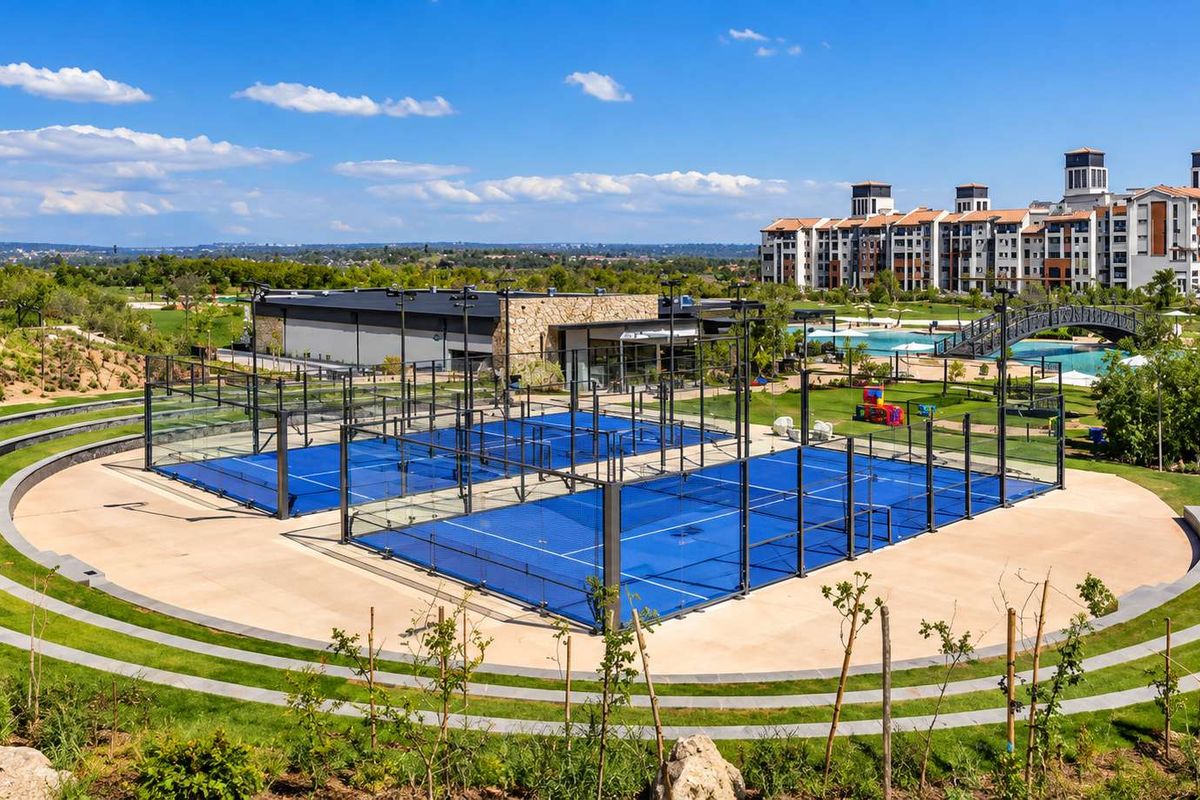 Well-maintained outdoor padel courts set within a landscaped recreational area, featuring modern floodlighting and paved surroundings.