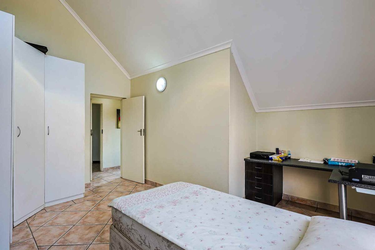 A bedroom featuring vaulted ceilings, tiled flooring, and built-in wardrobe storage, providing a functional and well-lit living space.