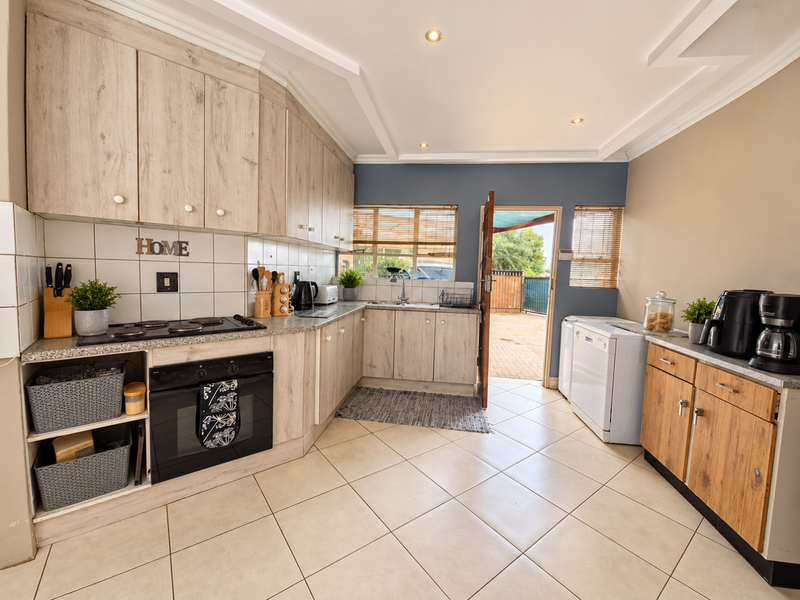 A functional kitchen featuring light wood-look cabinetry, tiled countertops, built-in oven and hob, and direct access to the rear outdoor area.
