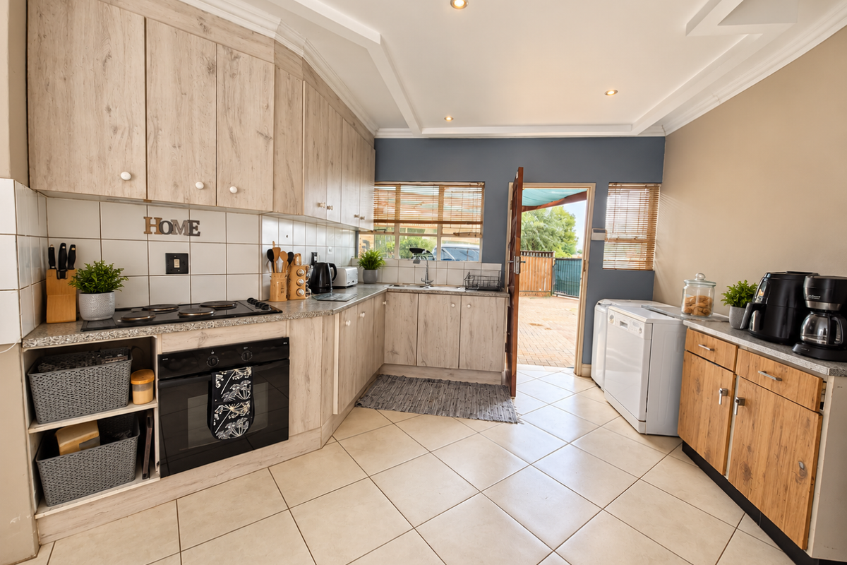 A functional kitchen featuring light wood-look cabinetry, tiled countertops, built-in oven and hob, and direct access to the rear outdoor area.