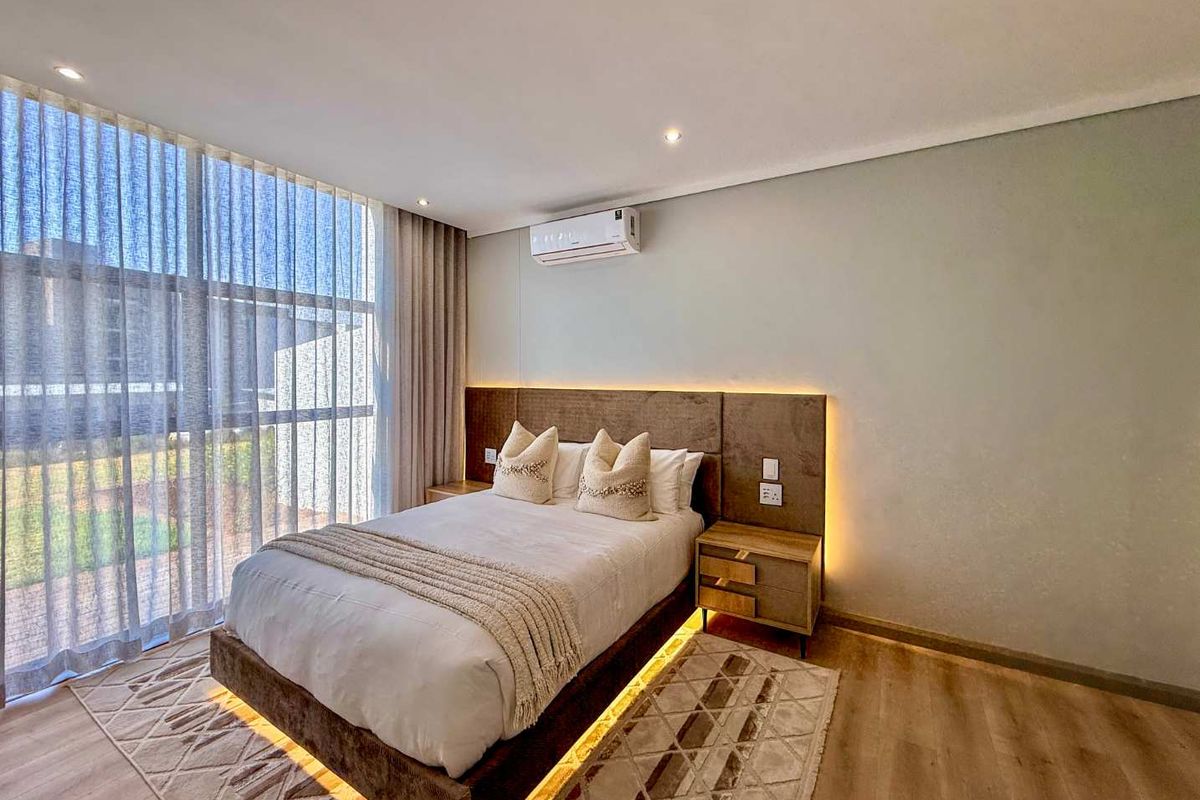 Modern bedroom featuring floor-to-ceiling windows, integrated headboard lighting, and a wall-mounted split-system air conditioner with high-quality laminate flooring.
