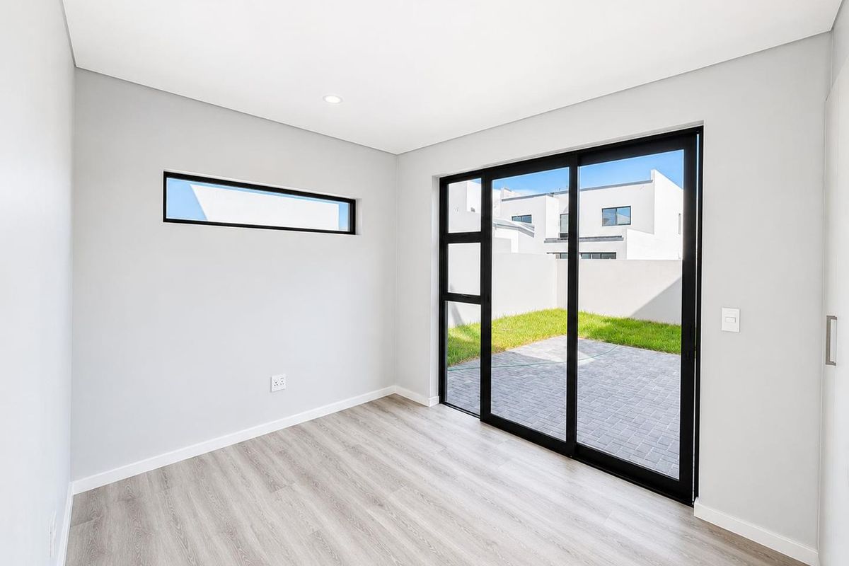 A bright, modern bedroom featuring light laminate flooring, a built-in cupboard, and large sliding glass doors providing direct access to a private paved patio.