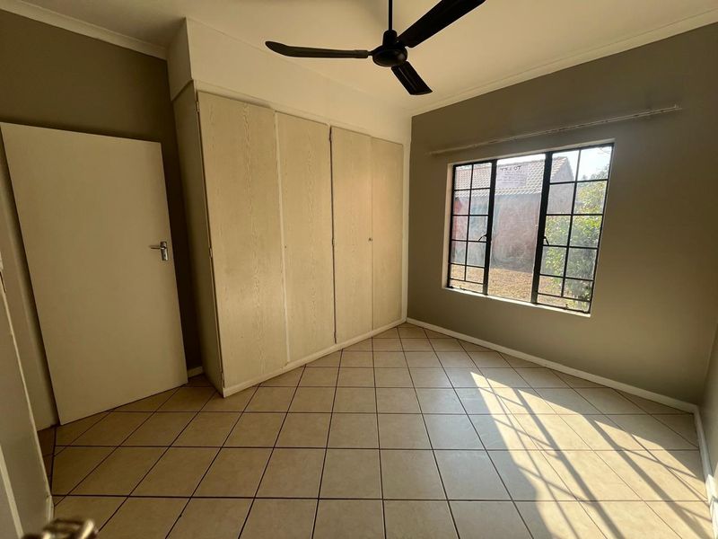 A bright, empty bedroom featuring tiled flooring, built-in cupboards, and a ceiling fan, offering a clean canvas for personalization.