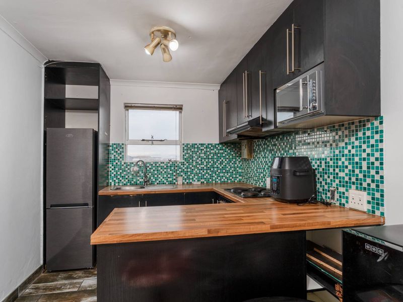 A compact kitchen featuring dark cabinetry, a wooden countertop, and a vibrant green mosaic tile backsplash with integrated appliances.