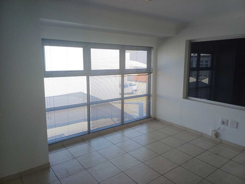 A bright, empty office space featuring large windows with venetian blinds and neutral tiled flooring, suitable for a professional workspace.