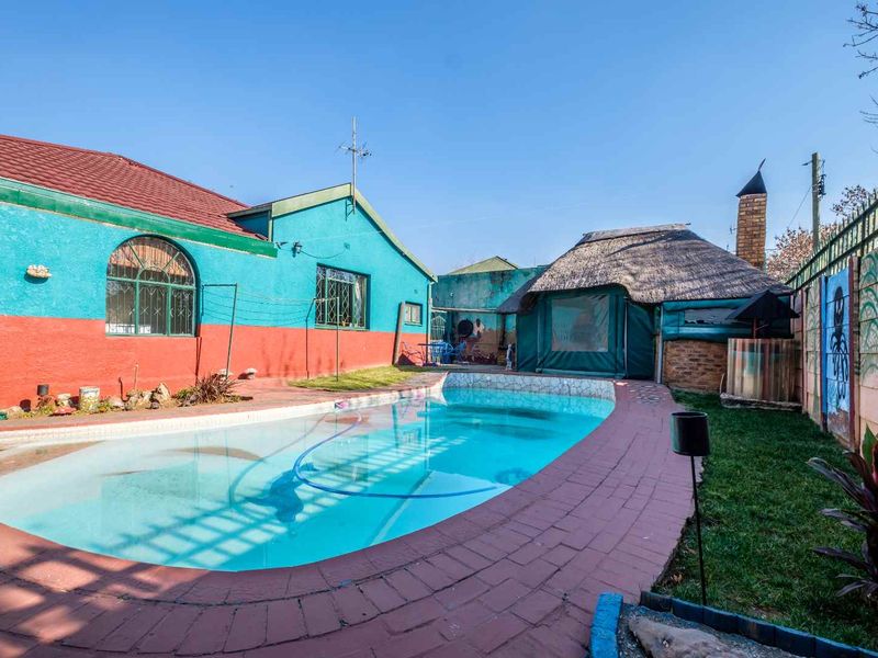 Outdoor entertainment area featuring a swimming pool, brick-paved surround, and a traditional thatched lapa with an integrated chimney.