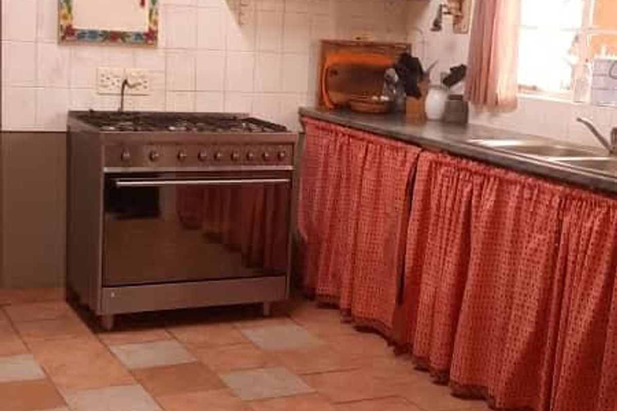 A functional kitchen featuring a freestanding gas stove, tiled splashbacks, open shelving, and a double sink with under-counter curtain storage.