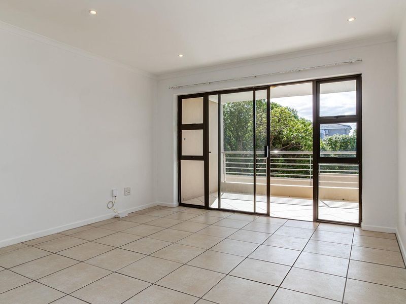 A bright, empty living room featuring neutral tiled flooring, recessed lighting, and large sliding glass doors that open onto a private balcony.