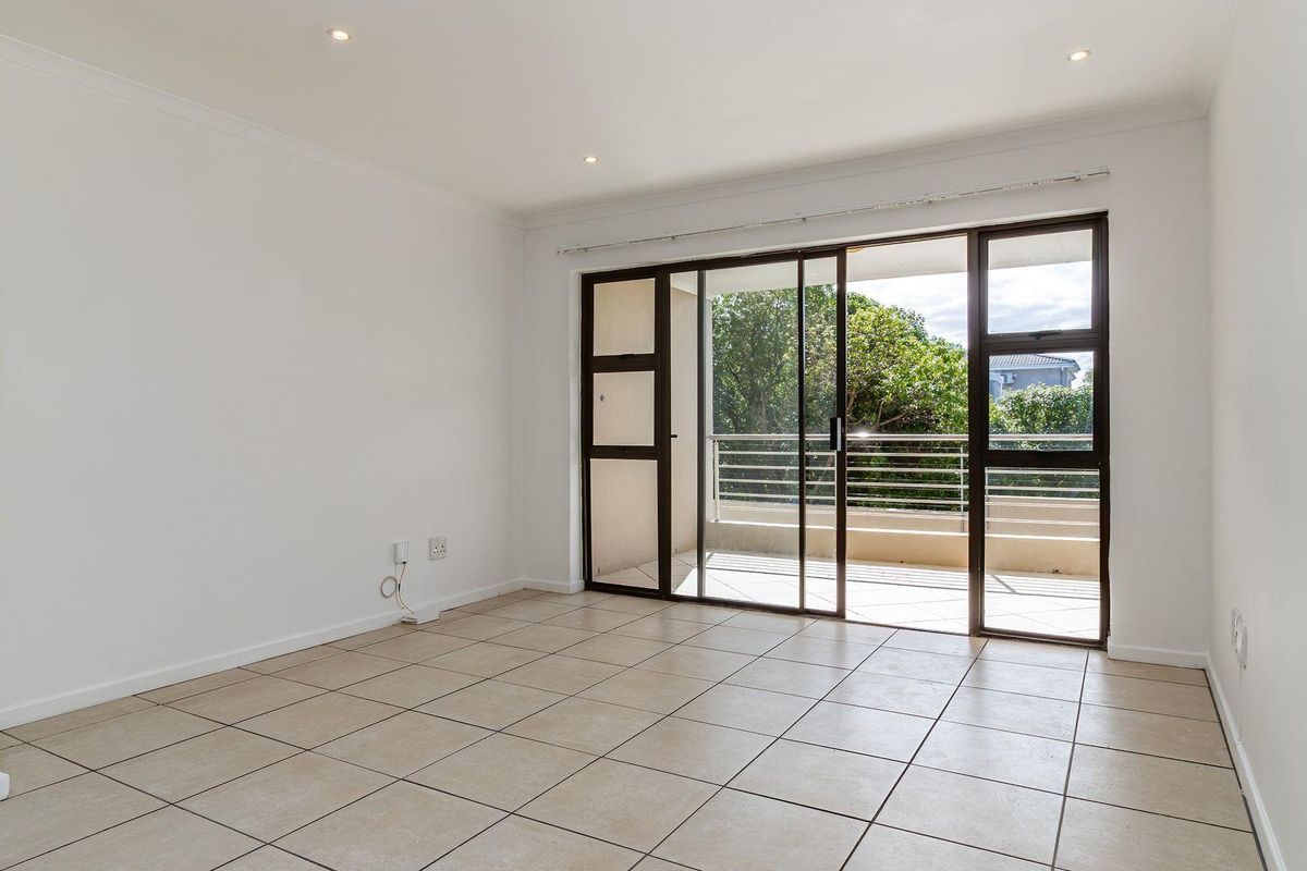 A bright, empty living room featuring neutral tiled flooring, recessed lighting, and large sliding glass doors that open onto a private balcony.