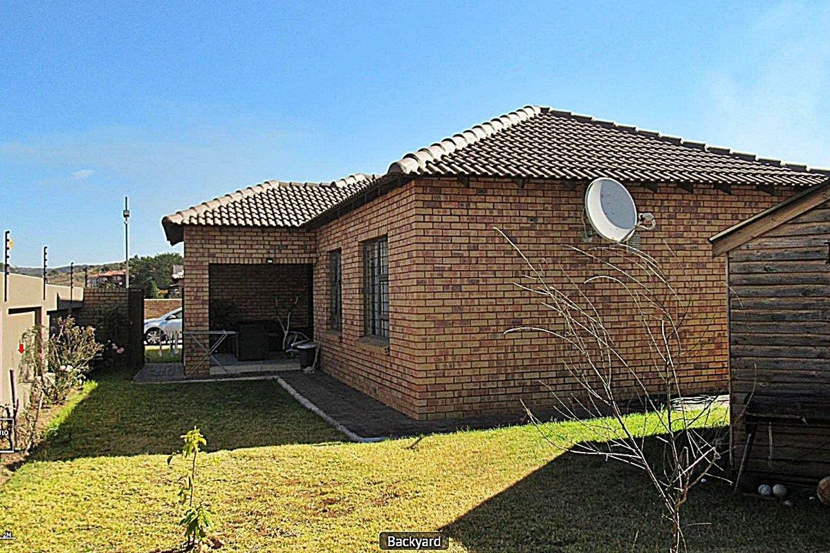 Rear view of the cluster home featuring a face brick exterior, tiled roof, and a covered patio area overlooking the garden.
