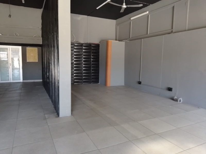 An open-plan retail space featuring tiled flooring, a dark exposed ceiling with a fan, and a modern partition wall.