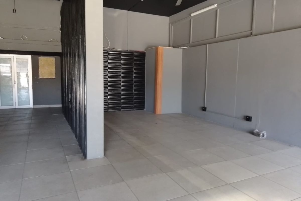 An open-plan retail space featuring tiled flooring, a dark exposed ceiling with a fan, and a modern partition wall.