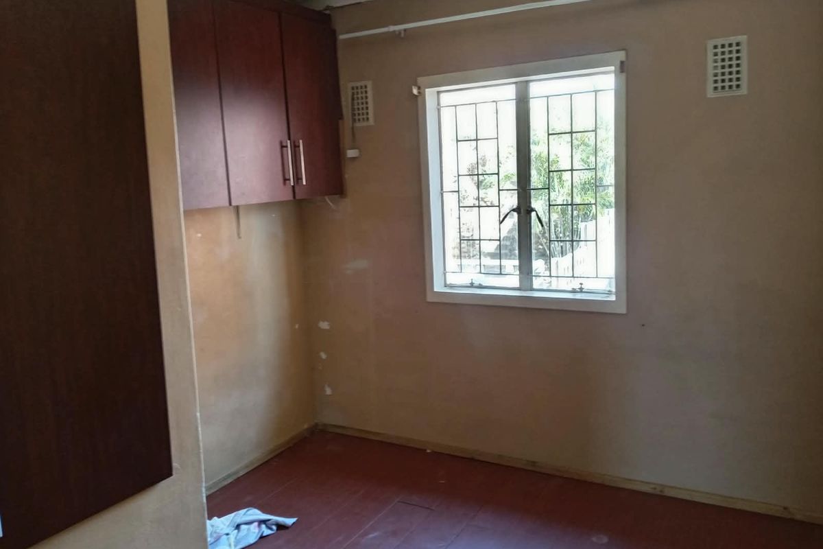 An empty bedroom featuring built-in cabinetry, security bars on the window, and ventilation grilles, requiring cosmetic updates to the walls and flooring.