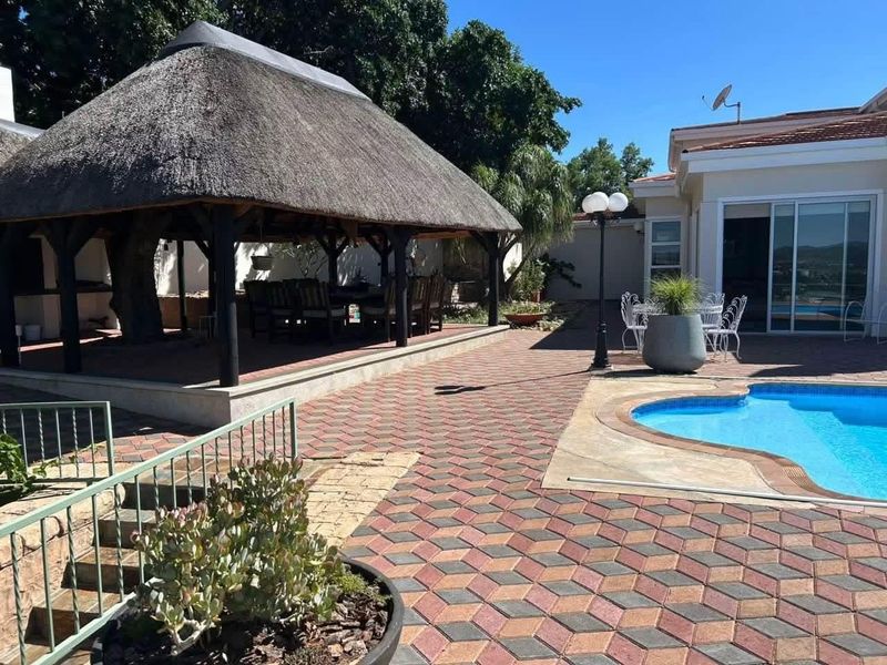 Outdoor entertainment area featuring a swimming pool, paved patio, and a large thatched lapa, perfect for hosting guests.