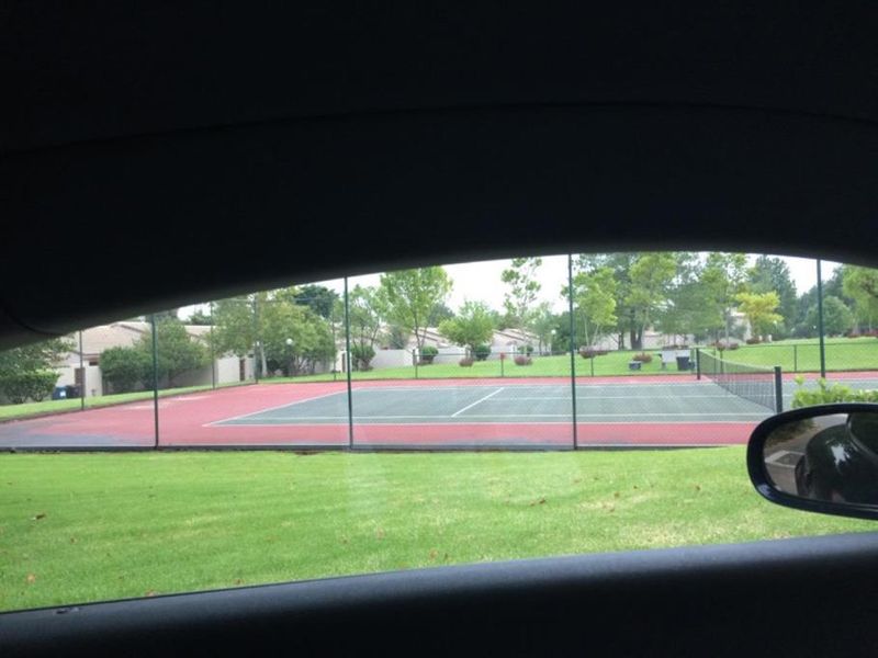 View of a communal tennis court facility with chain link fencing, captured from inside a vehicle.