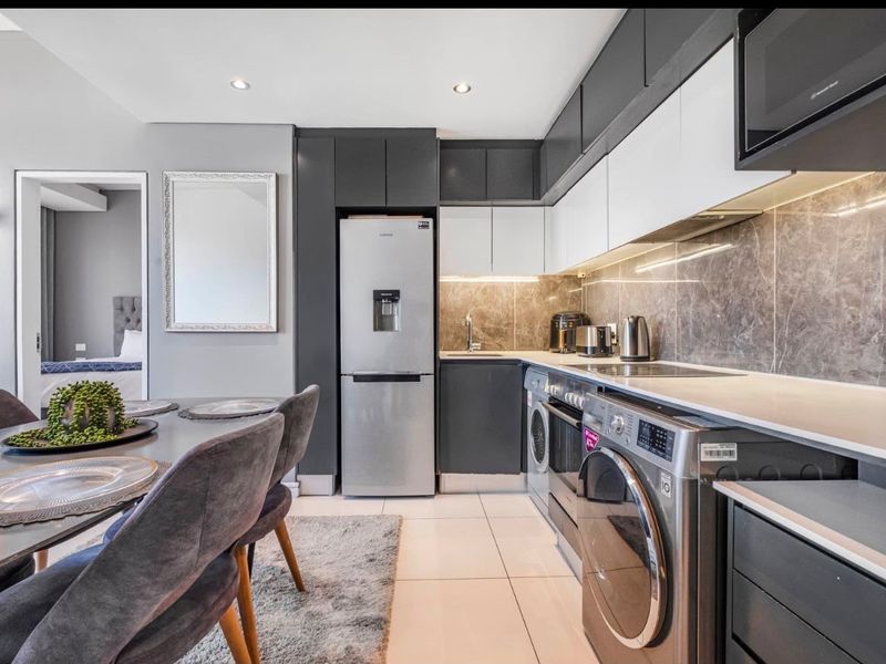 Modern open-plan kitchen featuring sleek two-tone cabinetry, stone-look backsplash, integrated appliances, and recessed lighting, seamlessly flowing into the dining area.