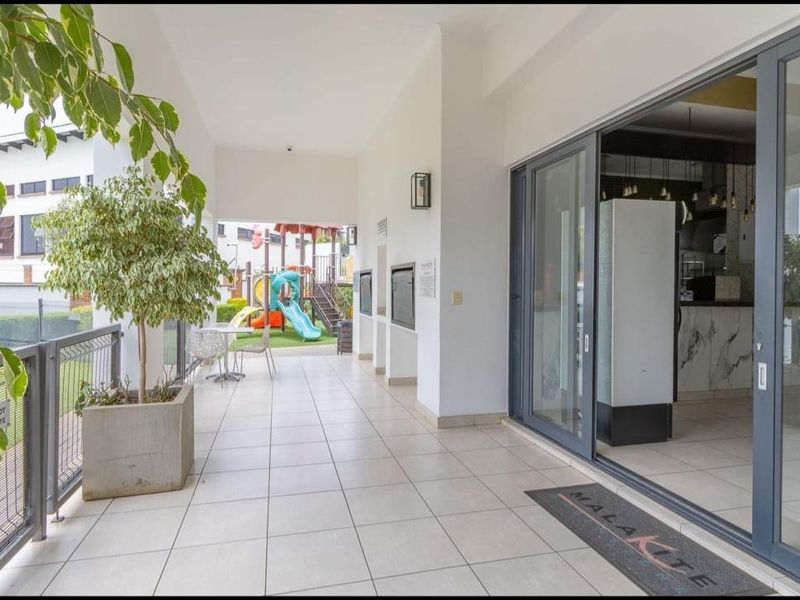A spacious covered patio featuring tiled flooring, a built-in braai, and large sliding glass doors providing seamless access to the interior living area.