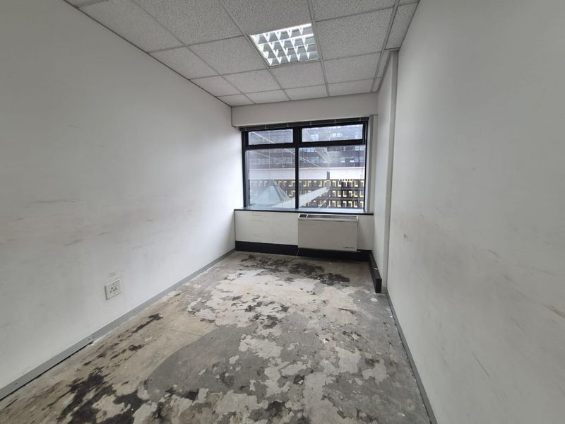 An empty office space featuring a suspended ceiling, recessed lighting, and an HVAC unit, currently requiring flooring and wall surface repairs.