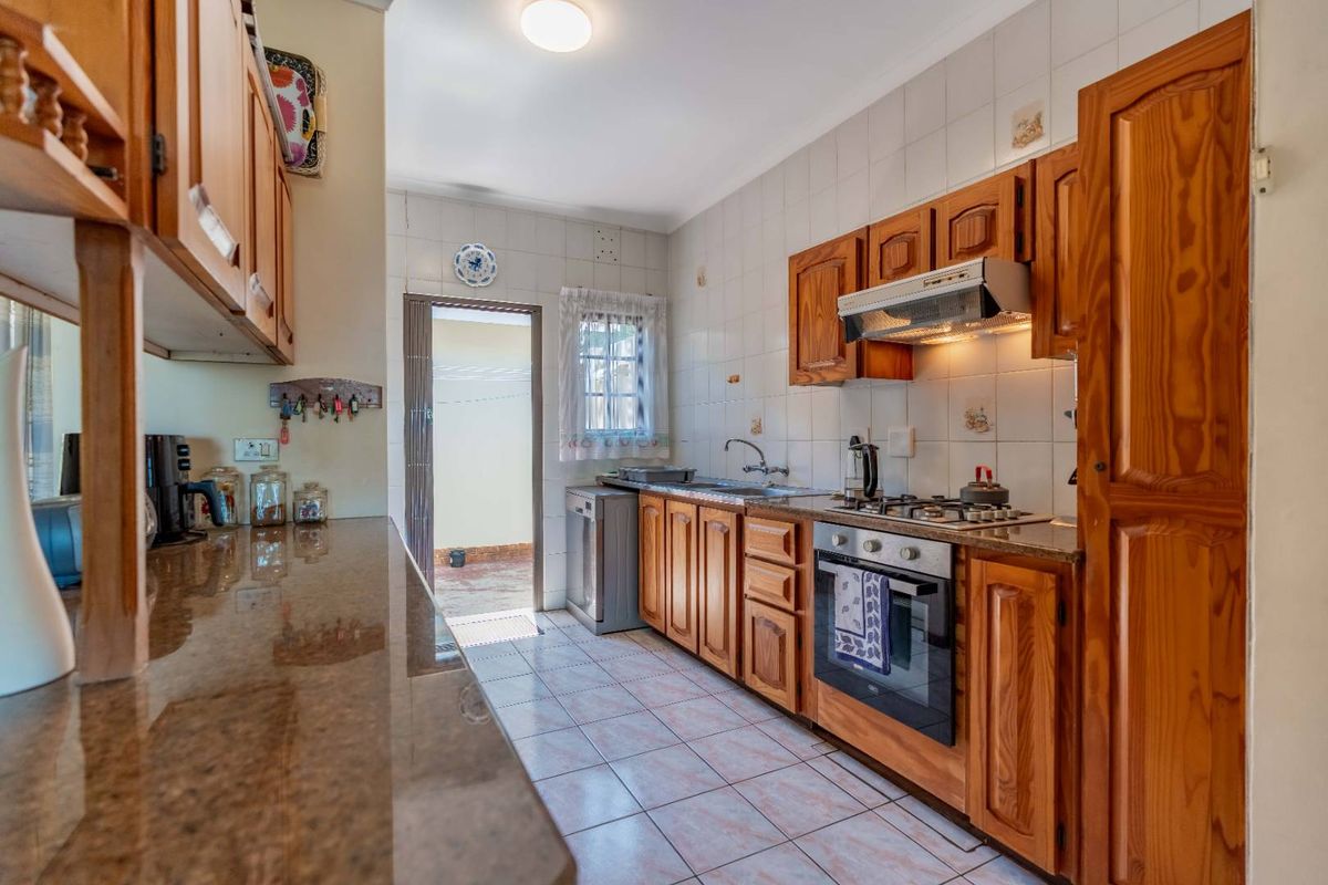 A functional kitchen featuring wooden cabinetry, granite countertops, a built-in oven, gas hob, and an extractor fan, with direct access to an outdoor area.