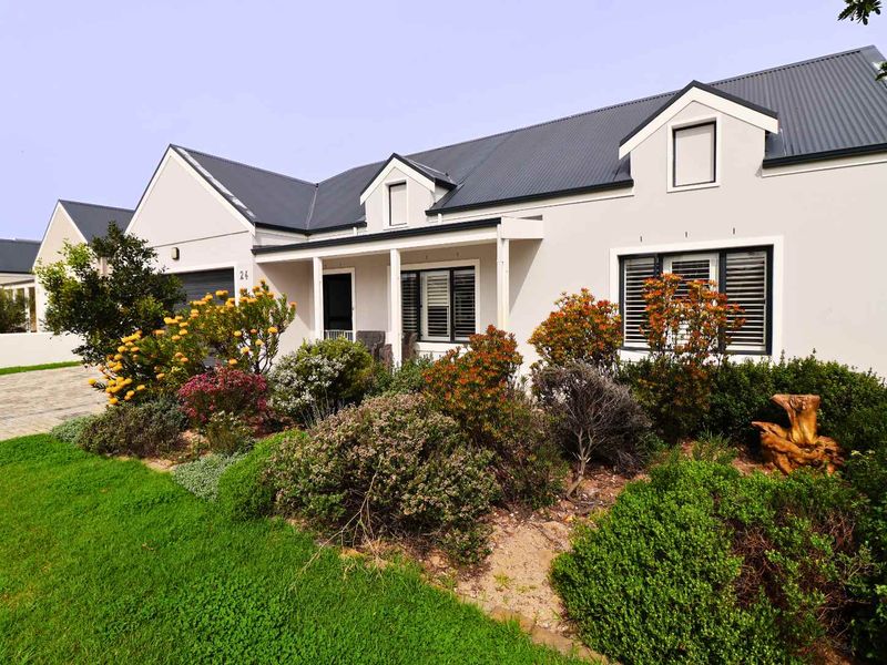 A well-maintained single-story residential home featuring a modern corrugated metal roof, dormer windows, and a neatly landscaped front garden.