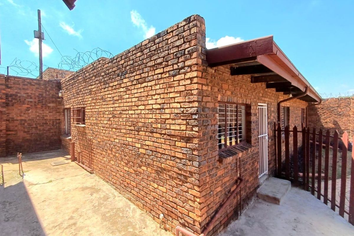 Exterior view of a face-brick residential building featuring security bars on windows and a concrete paved walkway.