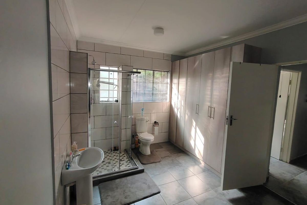 A functional bathroom featuring a glass-enclosed shower, pedestal sink, toilet, and extensive built-in cabinetry for storage, finished with neutral wall and floor tiling.