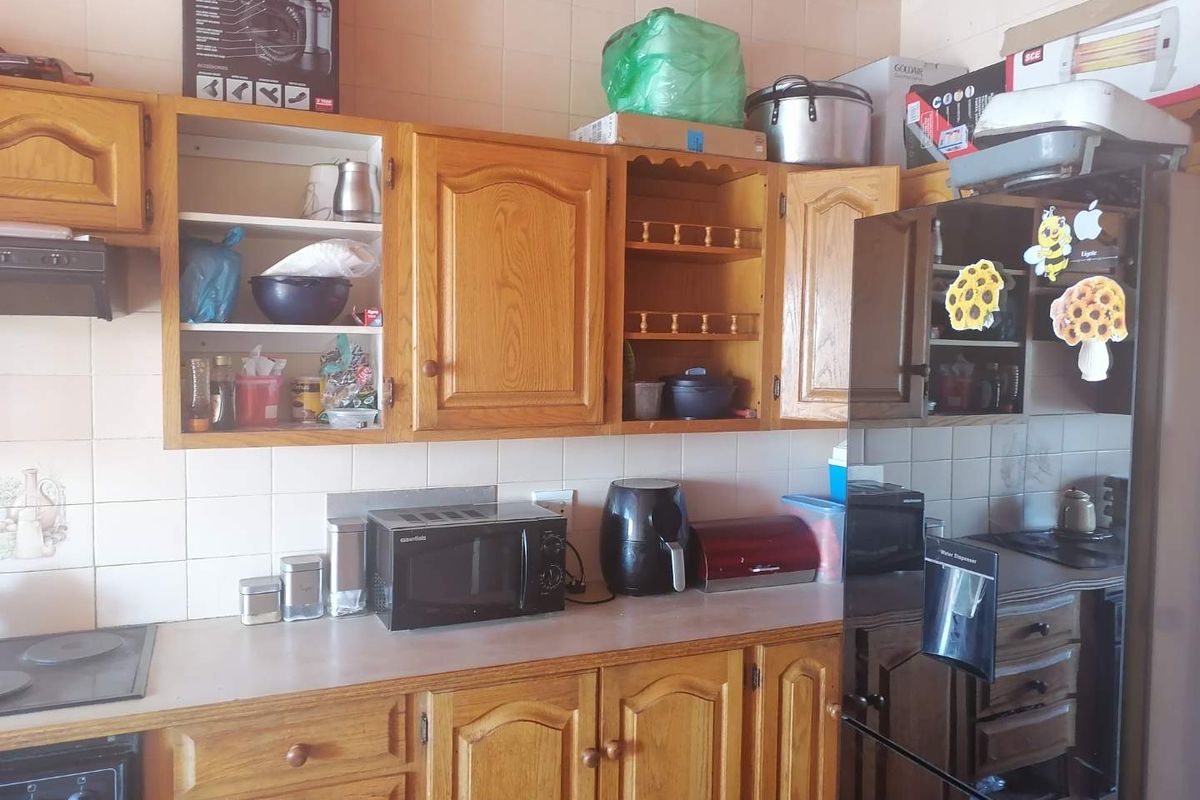 A dated kitchen featuring traditional wooden cabinetry, laminate countertops, and ceramic wall tiles, offering a functional layout with potential for modern renovation.
